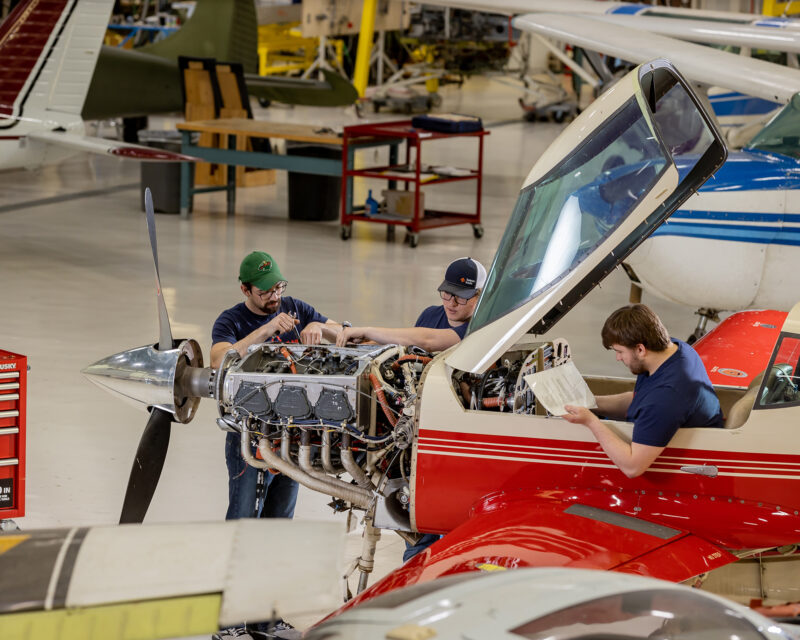 Aviation students working on a airplane engine in aerospace hangar.