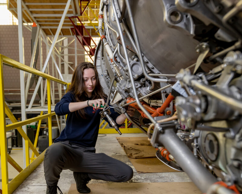 Female aviation student working on a airplane engine in aerospace hangar.